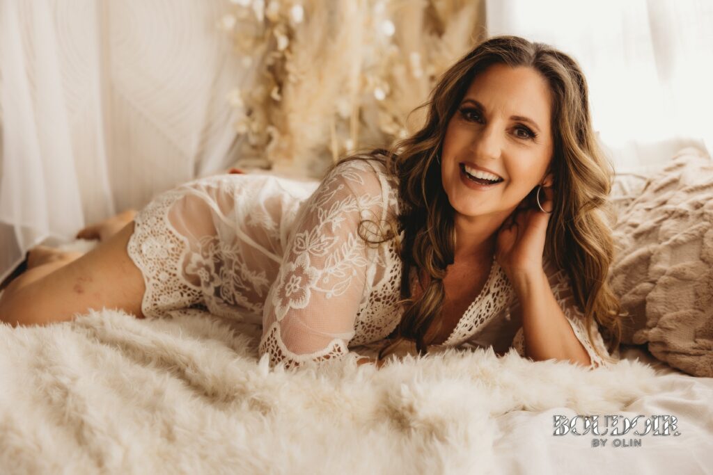 woman in lacy white robe on bed smiling for Sacramento boudoir photographer