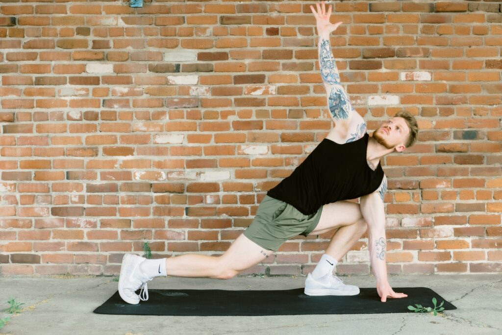 blonde man in black tank top, green shorts, practicing yoga in front of a brick wall embracing authenticity through sacramento dating photography