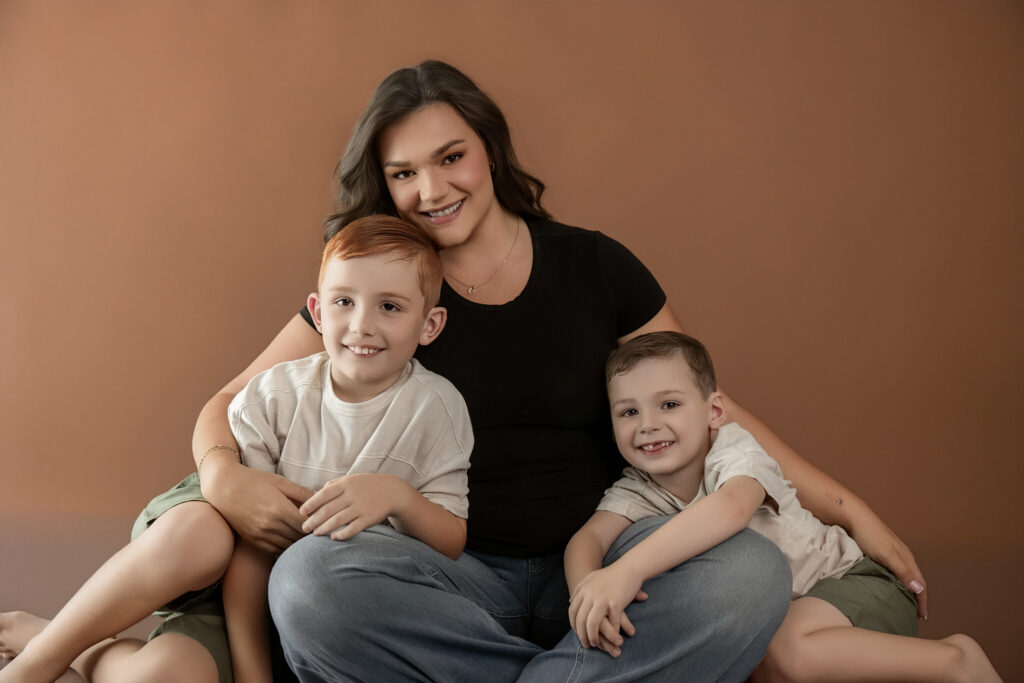 Mother sitting with her two young sons in a warm-toned studio portrait celebrating family connection and childhood memories in Sacramento.