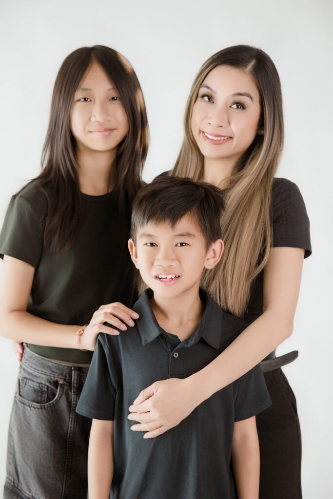 Mother embracing her son while standing with her daughter in a bright, modern Sacramento family photography studio portrait.