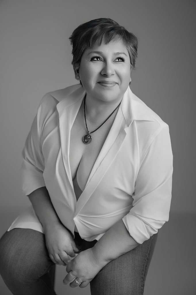 Beautiful black-and-white studio portrait of a smiling woman with short hair, wearing a white button-down shirt and pendant necklace during a breast cancer portrait session Sacramento.